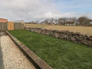 a stone wall next to a grassy field with a fence at Causeway Cottage in Berwick-Upon-Tweed