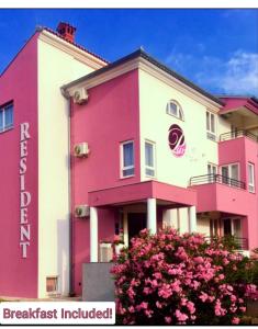 un edificio rosa y blanco con un arbusto delante de él en Residence Panolija, en Fažana