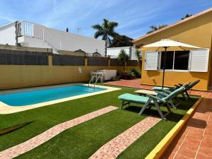 a backyard with a swimming pool with chairs and an umbrella at Casa Lube in Corralejo