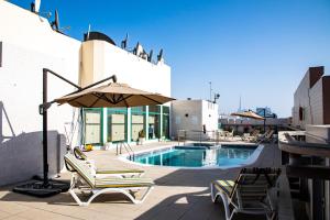un patio con sillas y una sombrilla junto a la piscina en West Zone Pearl Hotel Apartment, en Dubái