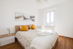 a white bedroom with a bed with yellow pillows at A terrace on the lake of Lugano in Aldesago