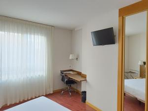 パレンシアにあるHotel Palacio Congresosのベッド、デスク、テレビが備わるホテルルームです。