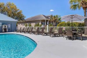 una piscina con sillas, una sombrilla y una casa en Comfort Suites Southport - Oak Island, en Southport