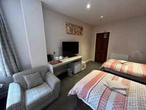Cette chambre comprend deux lits, une chaise et une télévision. dans l'établissement Acer Lodge Guest House, à Édimbourg
