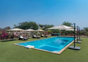a swimming pool with chairs and umbrellas at SaffronStays Brunton House, Alibaug - luxury pool villa near Awas Beach in Alibaug