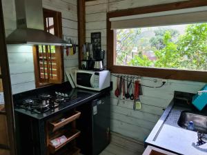 una cucina con forno a microonde, piano cottura e finestra di Chalé Paúba 80m do Mar a Pauba