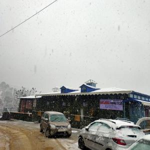 a snow covered street with cars parked in front of a store at Aasara HomeStay Soli Kausani in Kausani