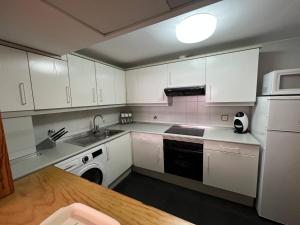 cocina con armarios blancos, fregadero y lavavajillas en Apartamento Muga, en Jaca