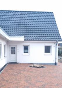 ein weißes Haus mit einem schwarzen Dach und einer steinernen Einfahrt in der Unterkunft Fewo Voßeler in Büsum