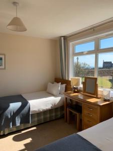 a bedroom with two beds and a desk and a window at Martyrs Bay Rooms in Iona