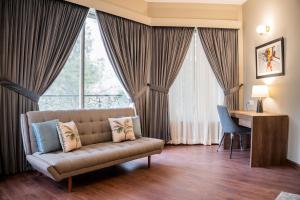 ein Wohnzimmer mit einem Sofa, einem Schreibtisch und Fenstern in der Unterkunft Hillside Residence E-7 by Paramount Hospitality in Islamabad