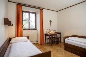 Cette chambre comprend 2 lits, une table et une fenêtre. dans l'établissement Gästehaus Benediktinerstift Göttweig - Bed & Breakfast Monastery, à Furth
