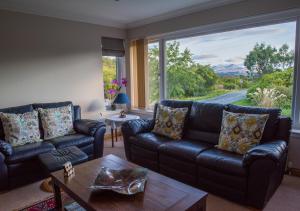 a living room with black leather couches and a large window at The Roses B&B in Portree