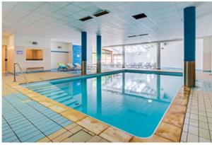 a large swimming pool with blue water in a building at La Croix du berger - Nid douillet été comme hiver in La Féclaz