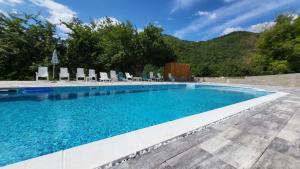 a swimming pool with chairs and trees and mountains at M&M Bazen resort Goražde in Goražde