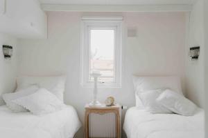 1 dormitorio con 2 camas con sábanas blancas y ventana en Brocante Holiday Home aan de bosrand! en Ermelo