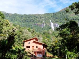 a house in the mountains with a waterfall in the background at Casa Cacau Boutique B&B - Sítio Salamandra Vale do Matutu in Aiuruoca