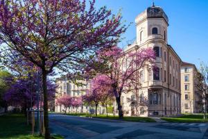 a building with a tower and trees with purple flowers at [Porta Nuova - Alpitour] Free Parking & Netflix in Turin