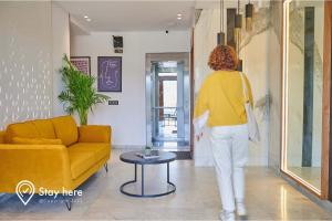 Eine Frau geht durch ein Wohnzimmer mit einer gelben Couch. in der Unterkunft Stayhere Rabat - Hay Riad - Sophisticated Residence in Rabat