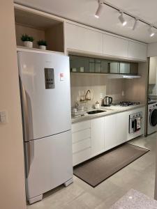 una cucina bianca con frigorifero e piano cottura di Apartamento Centro Vitta Boulevard a Gramado
