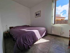 ein Schlafzimmer mit einem Bett mit einer lila Decke und einem Fenster in der Unterkunft Appart tout à portée de tongs! in Mimizan