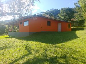 ein kleines orangenes Haus auf einem Grasfeld in der Unterkunft Casa Aconchegante Na Mantiqueira in Gonçalves