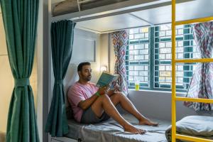 Ein Mann, der auf einem Bett sitzt und ein Buch liest. in der Unterkunft Whoopers Hostel Anjuna, Goa in Anjuna