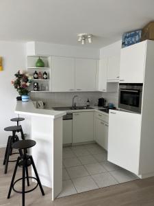 a white kitchen with white cabinets and stools at Blankeduyn Koksijde in Koksijde