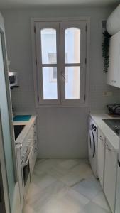 a white kitchen with a window and a washing machine at apartamento gaditano in Cádiz