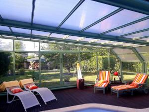 een afgeschermde veranda met stoelen en een zwembad bij Chambre d'hôte avec piscine couverte in Coulaines