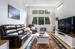 a living room with a leather couch and a flat screen tv at The Yellow Door Inverloch in Inverloch