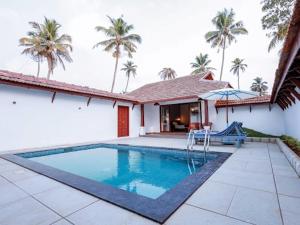 a swimming pool in front of a house with palm trees at Abad Turtle Beach in Mararikulam