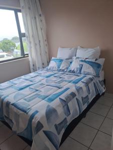 a bed with a blue and white comforter and a window at 3The Olive Complex Richards Bay 3900 in Richards Bay