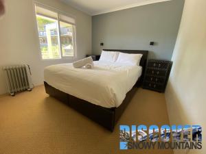 a bedroom with a large bed with white sheets and a window at Inala 3 in Thredbo