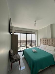 a bedroom with a bed with a green blanket and a chair at Makai - Nayarak Paracas in Paracas