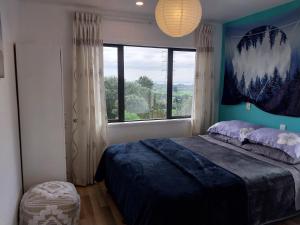 ein Schlafzimmer mit einem Bett und einem großen Fenster in der Unterkunft Cosy Country Cottage on a Sunny Hill in New Plymouth