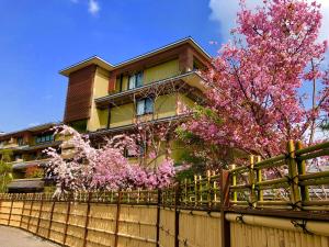 a house with a fence and a tree with pink flowers at Kadensho, Arashiyama Onsen, Kyoto - Kyoritsu Resort in Kyoto