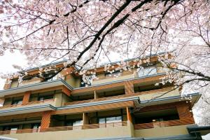a building with pink cherry trees in front of it at Kadensho, Arashiyama Onsen, Kyoto - Kyoritsu Resort in Kyoto