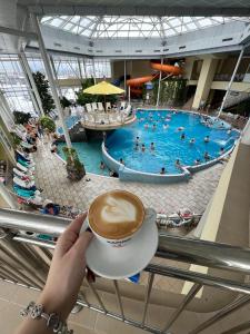 a person holding a cup of coffee in front of a swimming pool at Hotel Alinalex - Paradisul Acvatic in Braşov