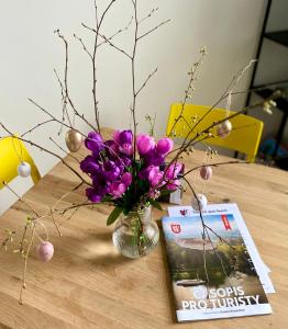 een vaas met paarse bloemen op een tafel met een tijdschrift bij Berta's Apartments in Děčín