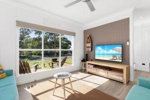 a living room with a flat screen tv and windows at Abode Callala Beach Jervis Bay - 100m to Beach! in Callala Beach
