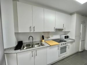 cocina con armarios blancos, fregadero y microondas en Apartamento en palmeira - Colores del Barbanza Naranja, en Ribeira