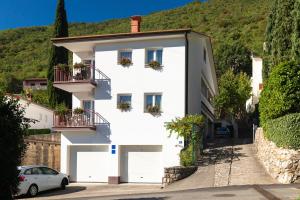 a white house with two balconies and a car at Apartmani Margita in Mošćenička Draga
