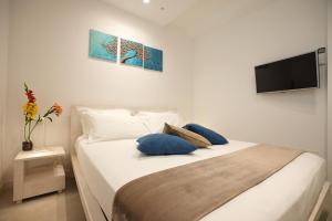 a white bed with blue pillows and a flat screen tv at Keys of Sicily - Marina di Modica in Marina di Modica