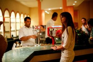 a woman standing in front of a bar with a bartender at Royal Lido Resort & Spa in El Fehri