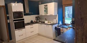 une cuisine avec des placards blancs et un mur bleu dans l'établissement La Poissonnais, à Saint-Lormel