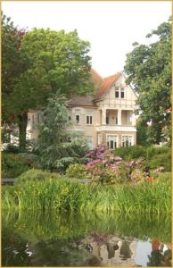 クックスハーフェンにあるVilla Deichvoigtの池前の木々と花々が咲き誇る大白い家