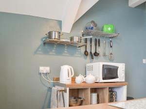 a kitchen with a microwave and a shelf with utensils at Spindrift in Coverack