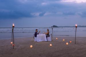 two people sitting at a table on the beach at Weligama Bay Marriott Resort & Spa in Weligama