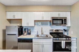 a kitchen with white cabinets and a stove and a sink at Get Comfy Memory Foam Beds and Tub in Central ATX in Austin